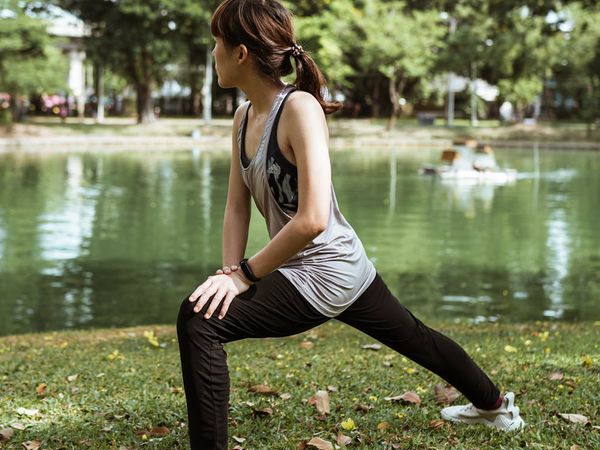 A woman in comfortable sportswear stretching outdoors in a sunny park.